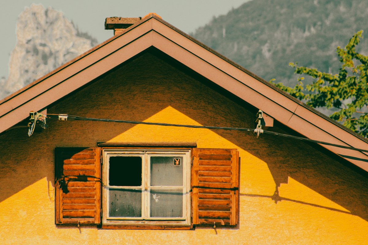 Façade de chalet jaune aux volets en bois, montagne en arrière-plan